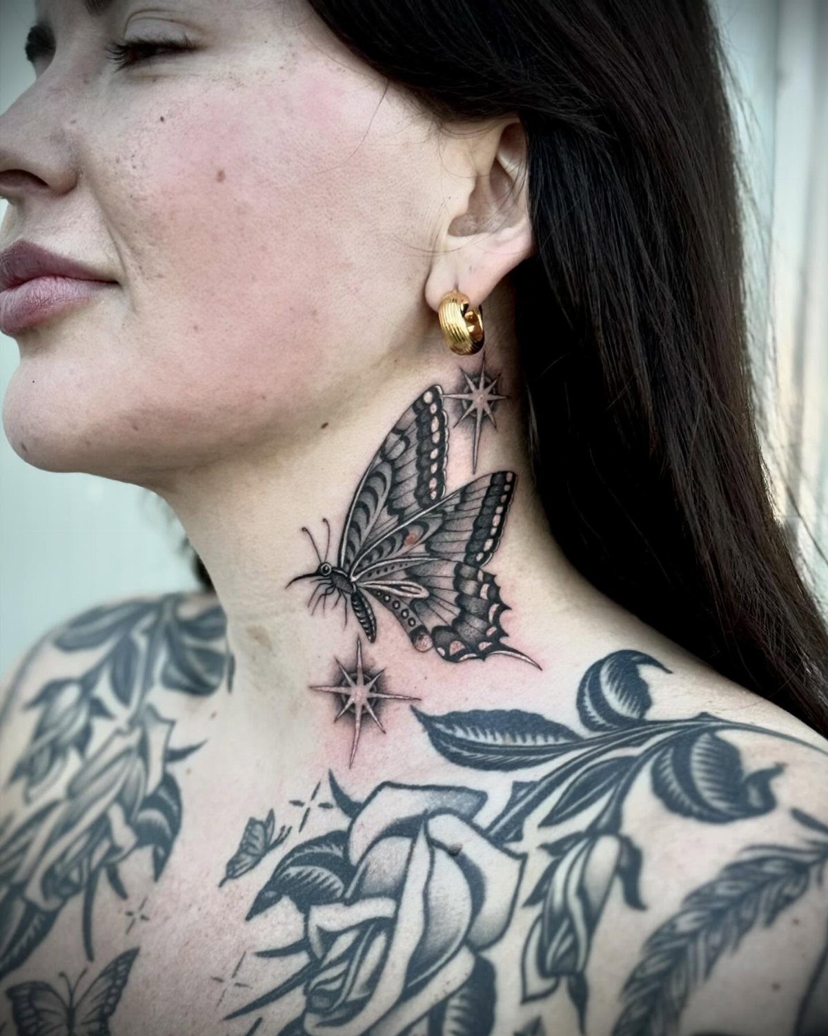 Butterfly tattoo with stars on a woman's neck and floral chest tattoos.