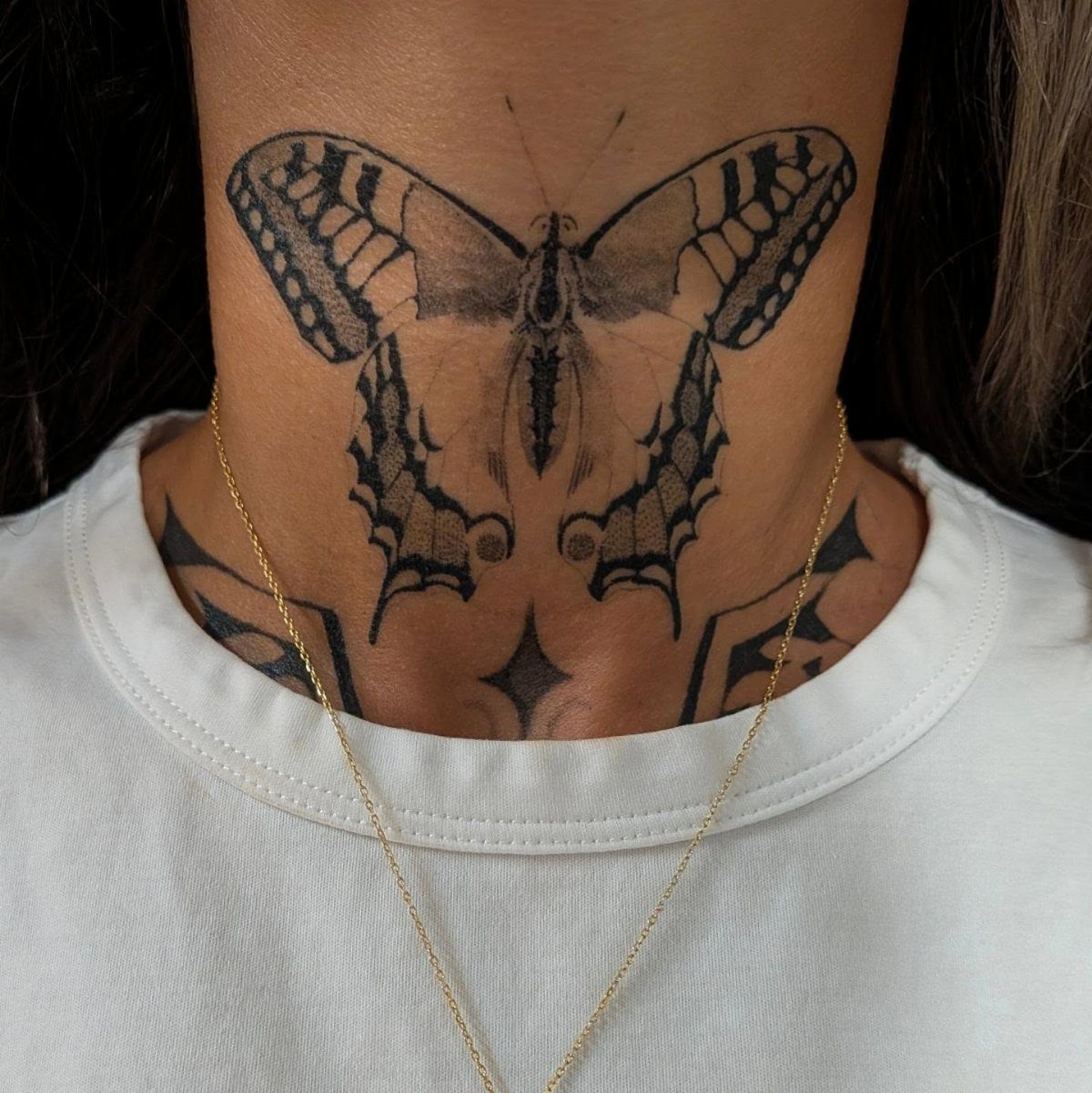 Black and gray butterfly tattoo centered on a person's neck above a white shirt