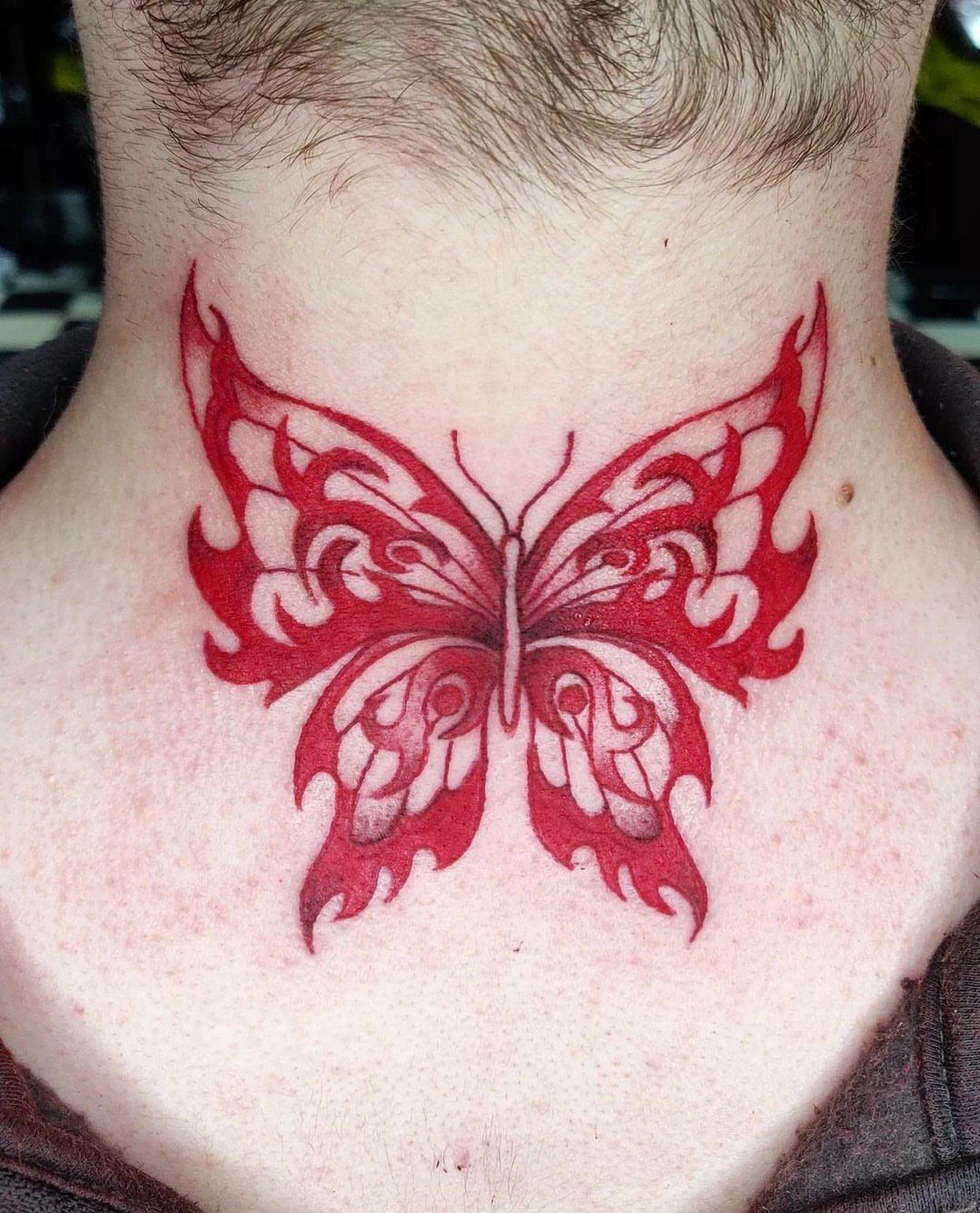 Red tribal butterfly tattoo centered on the back of a person's neck