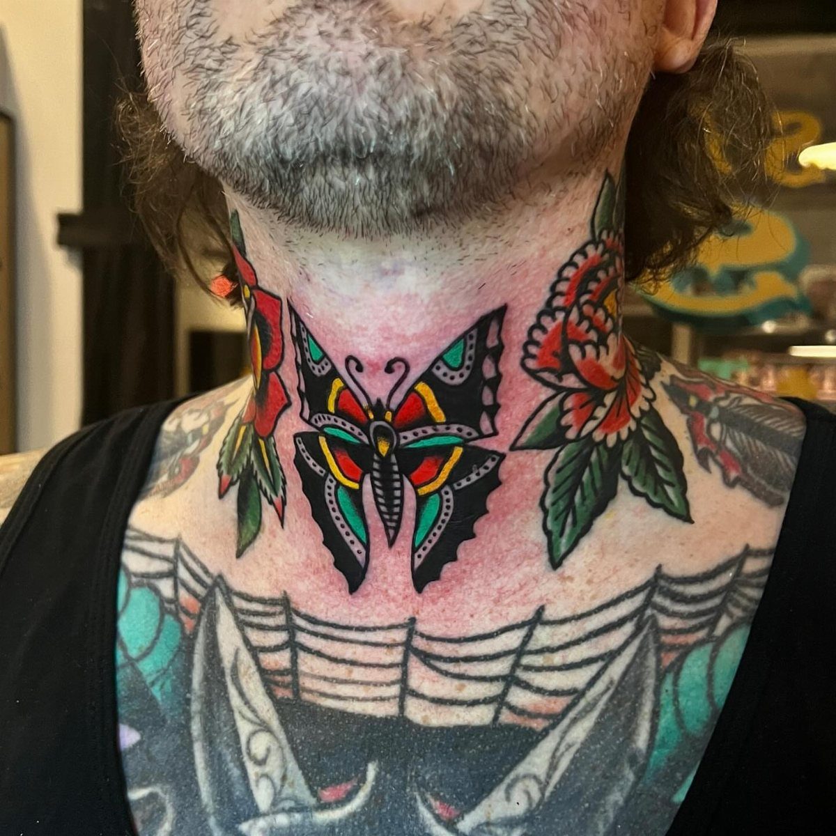 Vibrant traditional butterfly tattoo on a man's neck surrounded by red roses.