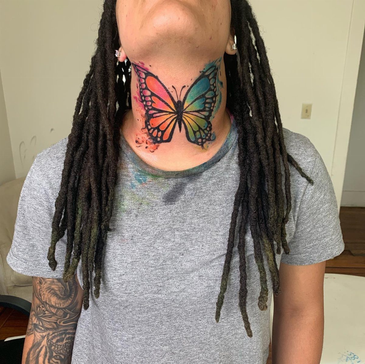 Colorful watercolor butterfly tattoo on the front of a person's neck