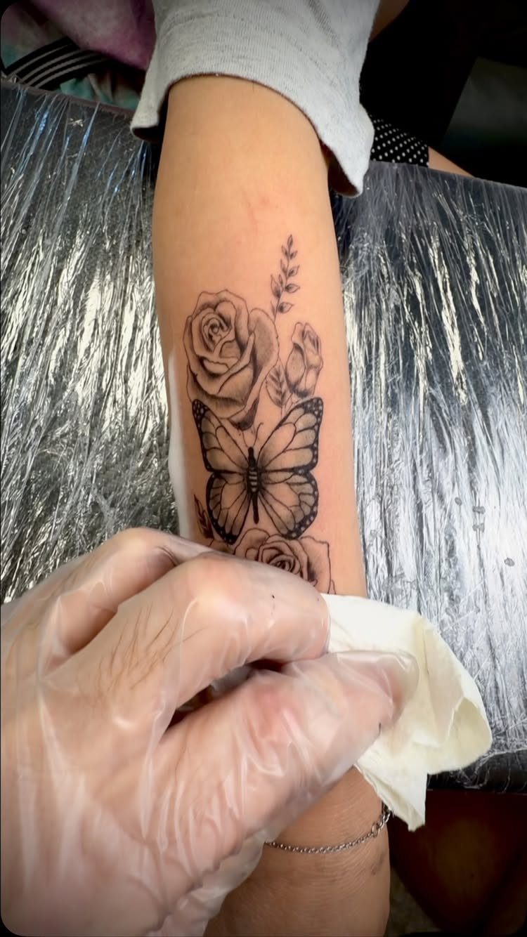 Black and gray tattoo of roses and a butterfly on a person's forearm.