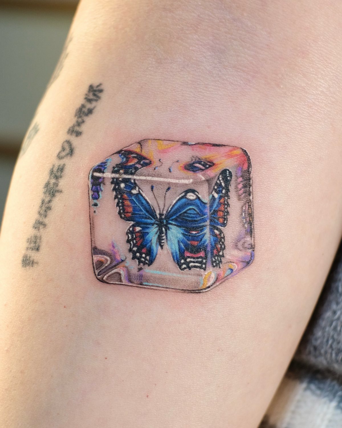 Blue butterfly tattoo encased inside a colorful translucent 3D ice cube on skin