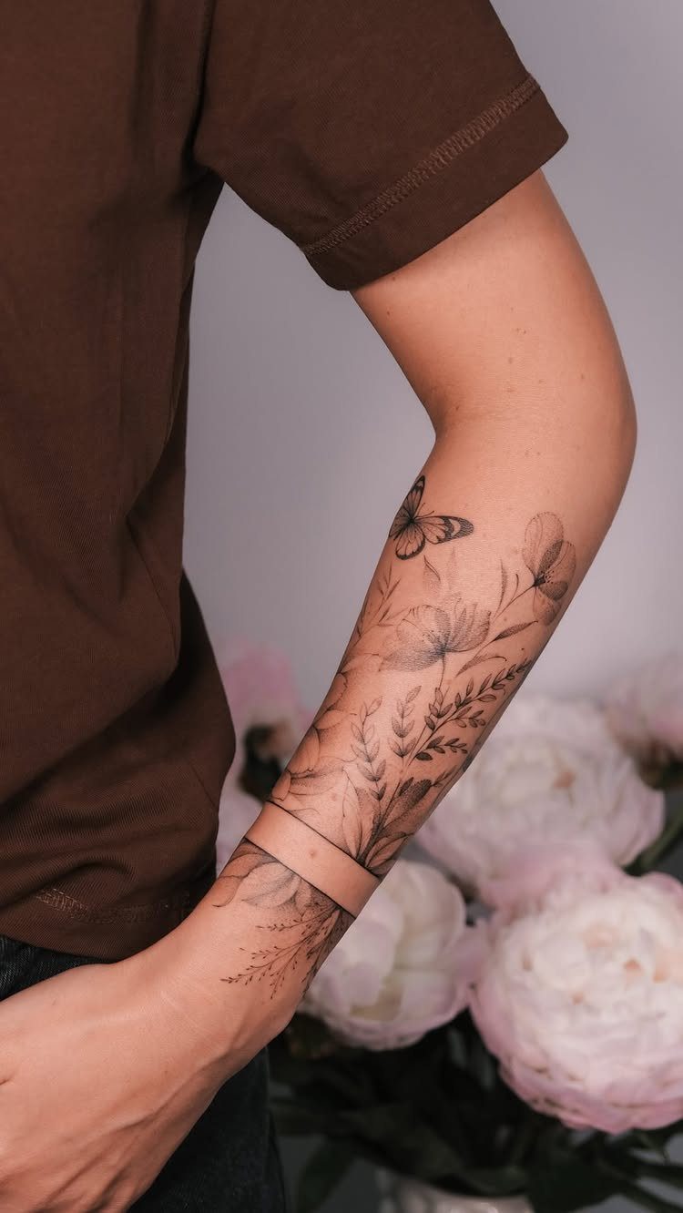 Forearm tattoo of a butterfly and delicate flowers in black ink.