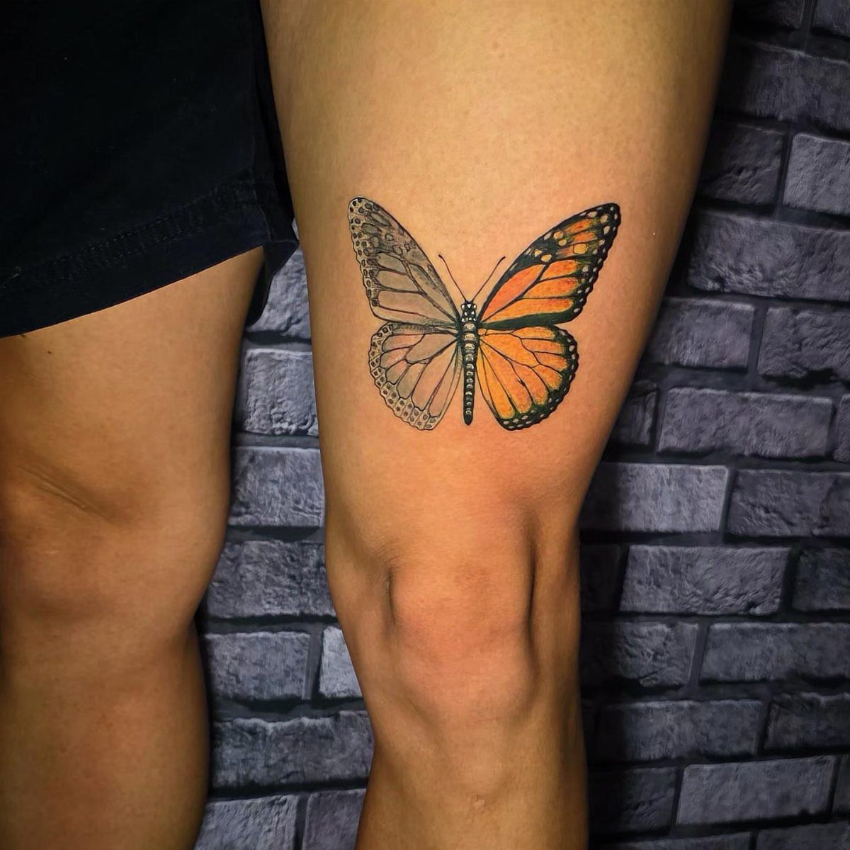 Butterfly tattoo on a thigh showing one black and grey wing and one orange wing