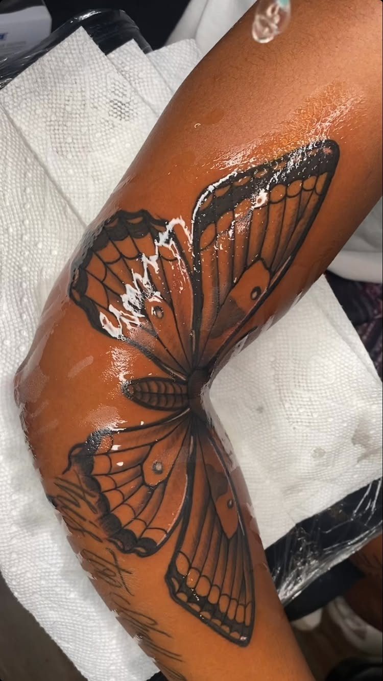 Large black ink butterfly tattoo spanning across a person's elbow and forearm.