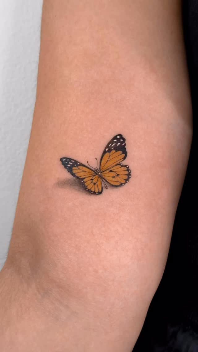 Small realistic orange butterfly tattoo with a 3D shadow on a forearm