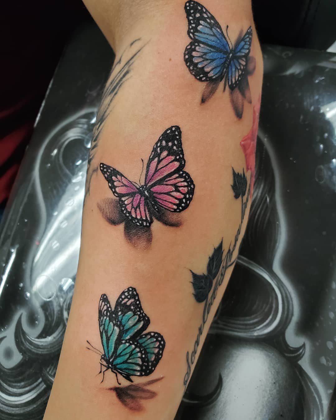 Three colorful 3D butterfly tattoos in blue, pink, and teal on a forearm.