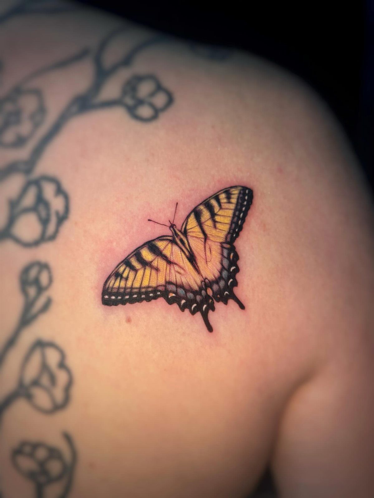 Yellow and black tiger swallowtail butterfly tattoo on a person's upper back.