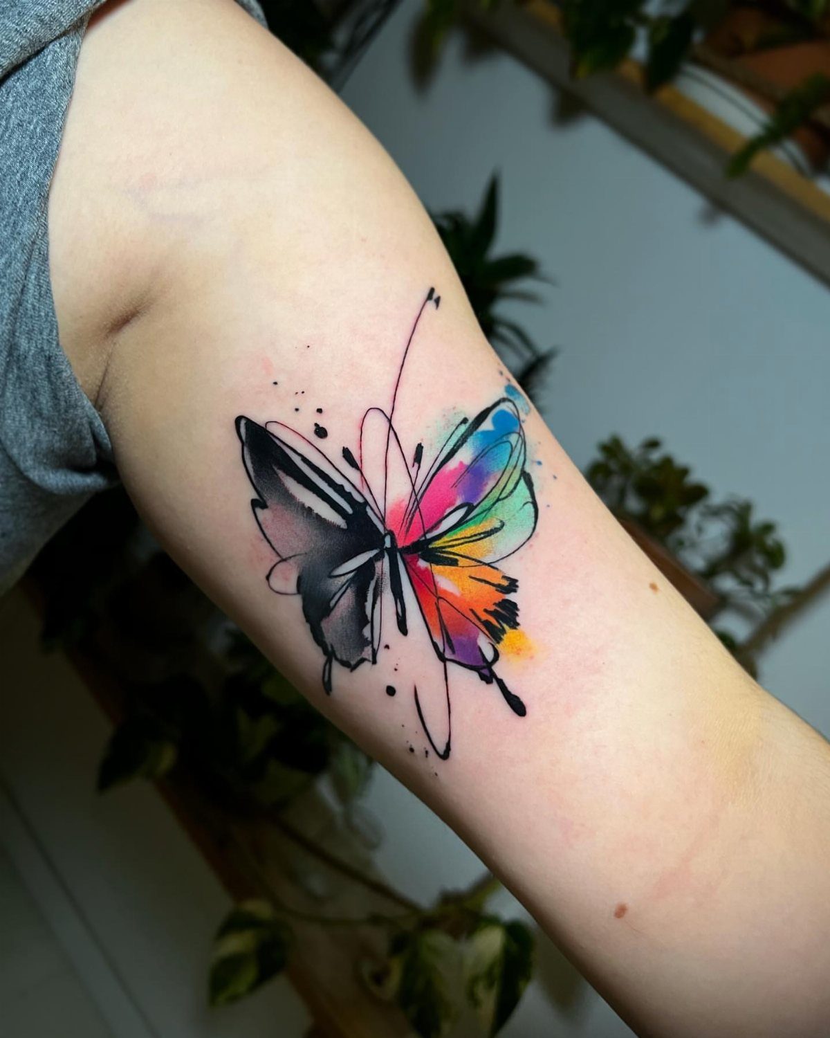 Watercolor butterfly tattoo on an arm with one colorful and one black wing.