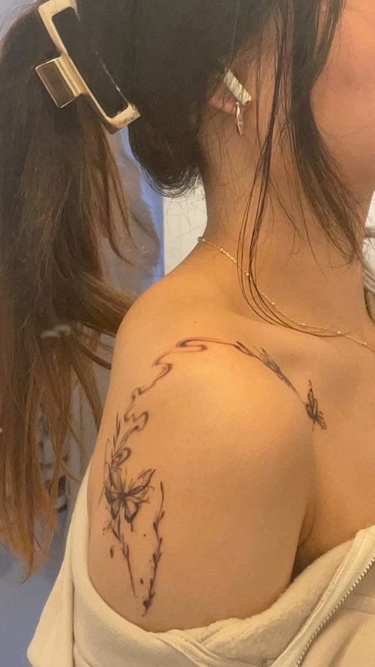 Butterfly tattoo on a shoulder with flowing abstract lines and asymmetrical design.