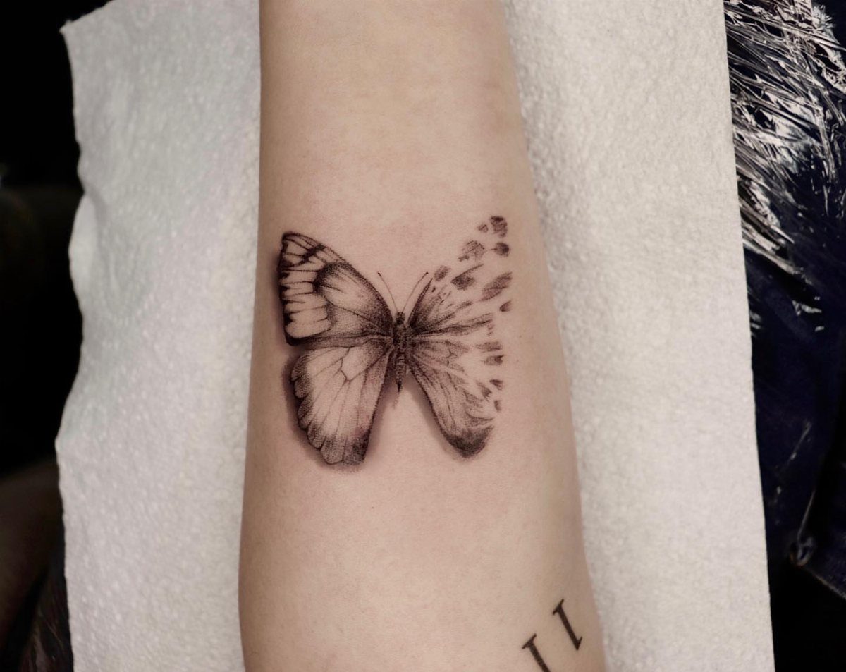 Butterfly tattoo on an arm with one wing dissolving into abstract fragments