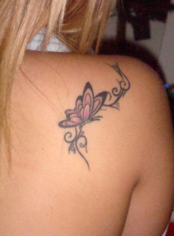 Butterfly tattoo with pink wings and black swirls on a person's shoulder