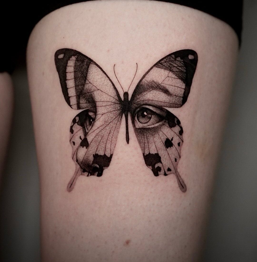 Butterfly tattoo on a shoulder featuring human eyes and faces within the wings.