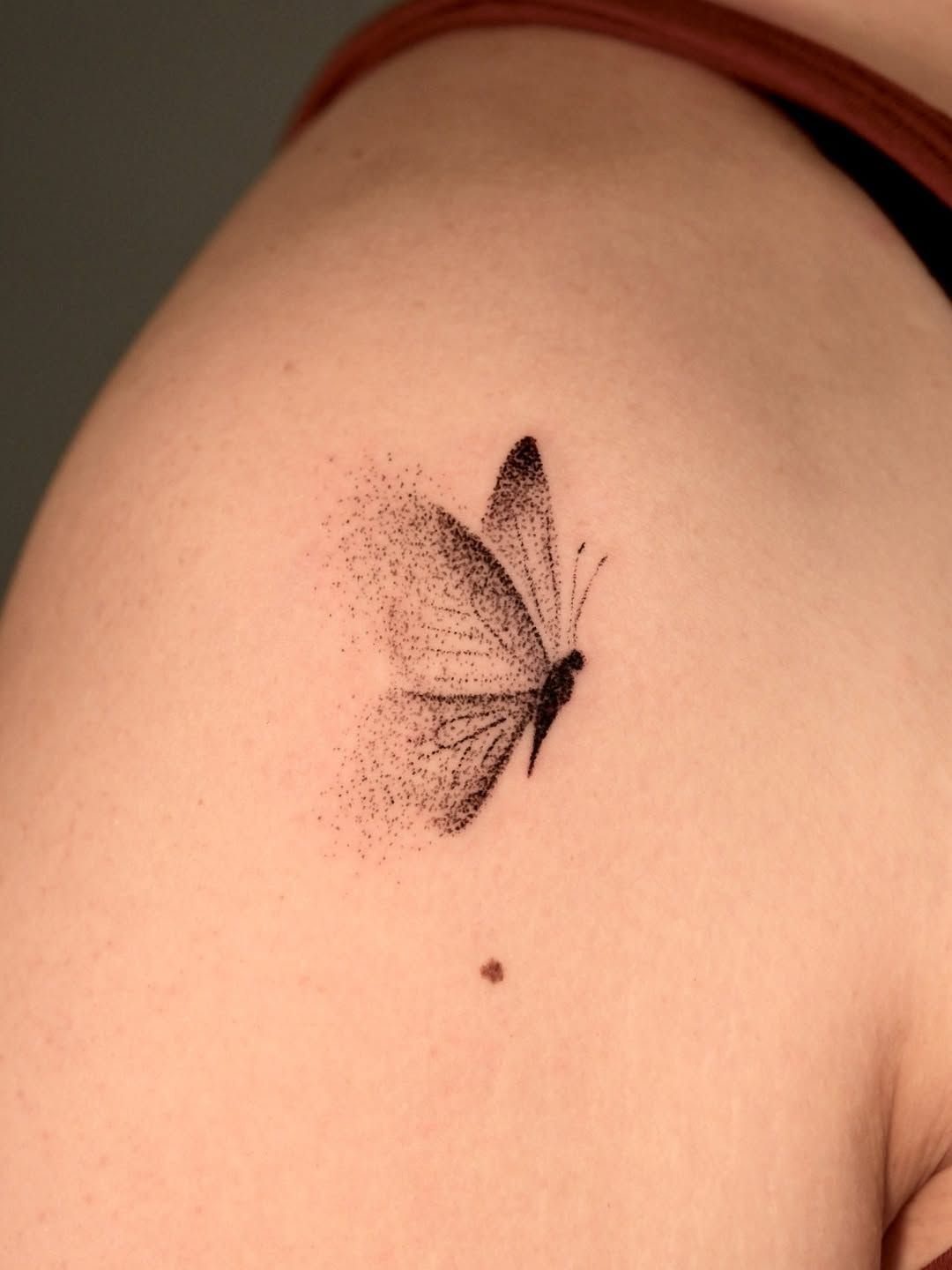 Butterfly tattoo on a shoulder with a stippled dot trail effect on one wing