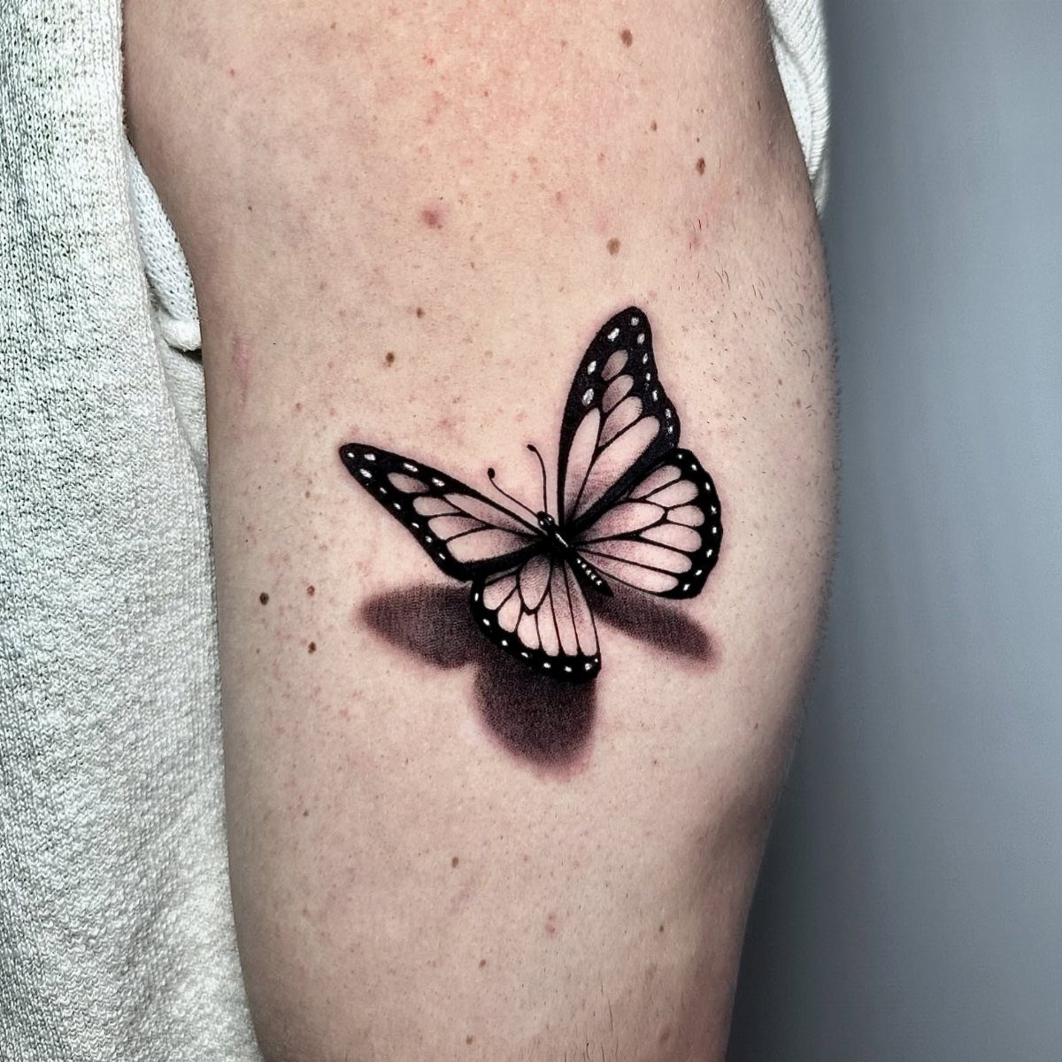 Butterfly tattoo on a shoulder with a realistic shadow creating a 3D effect.