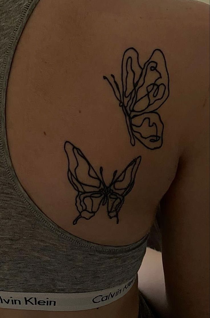 Two black ink butterfly tattoos with layered outlines on a person's shoulder.