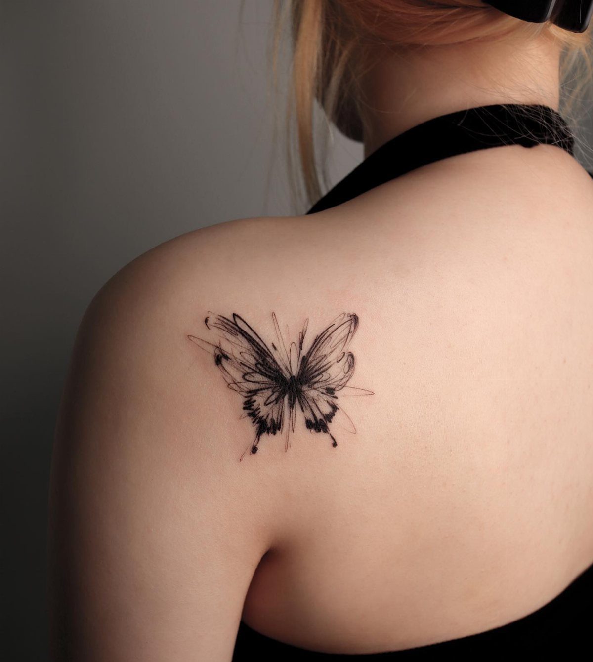 Sketchy black ink butterfly tattoo with artistic lines on a person's shoulder