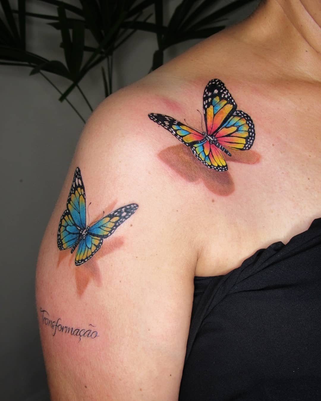Two colorful butterfly tattoos on a shoulder with soft airbrushed shadows underneath them.