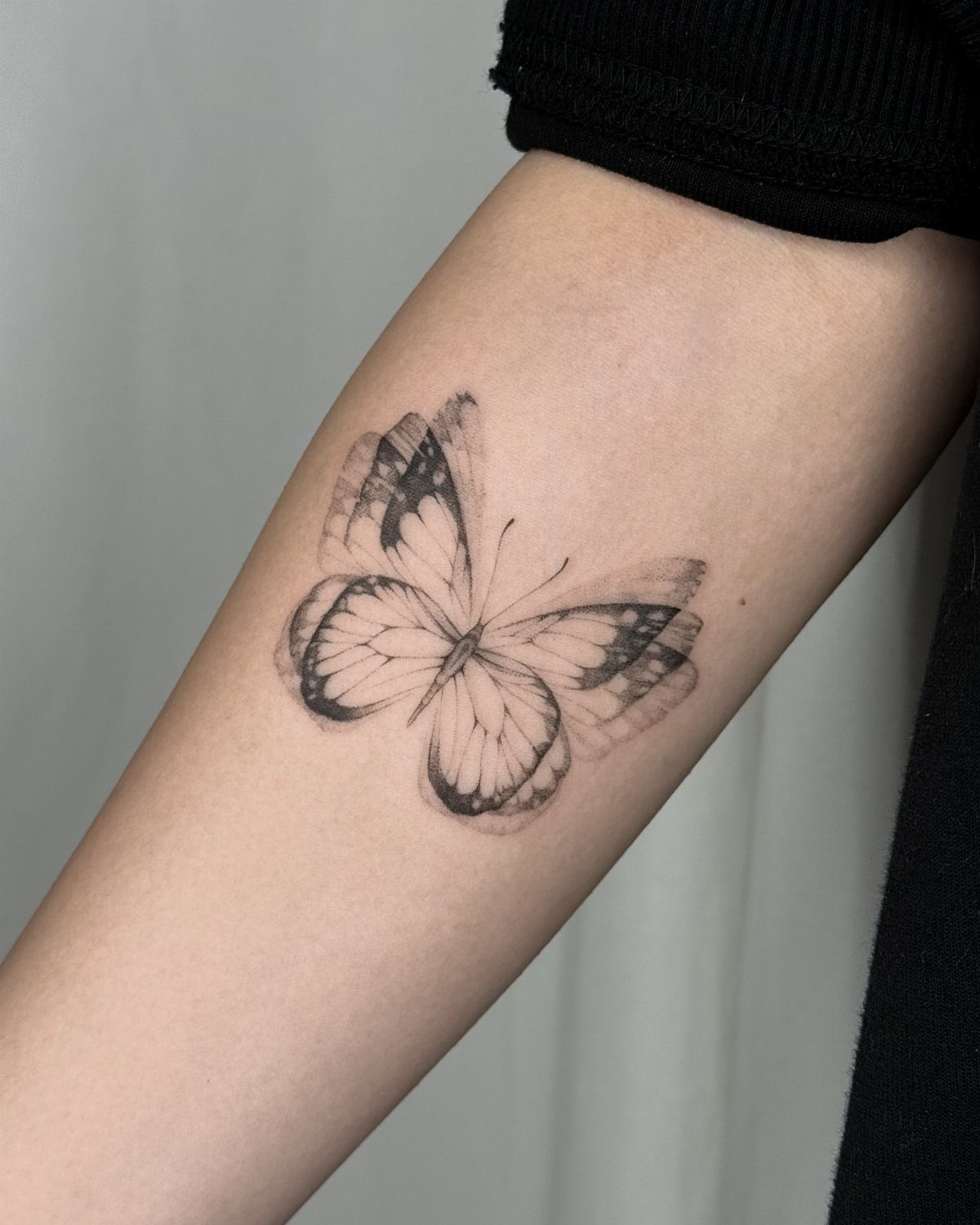 Butterfly tattoo on a shoulder with blurred wing effects suggesting motion.