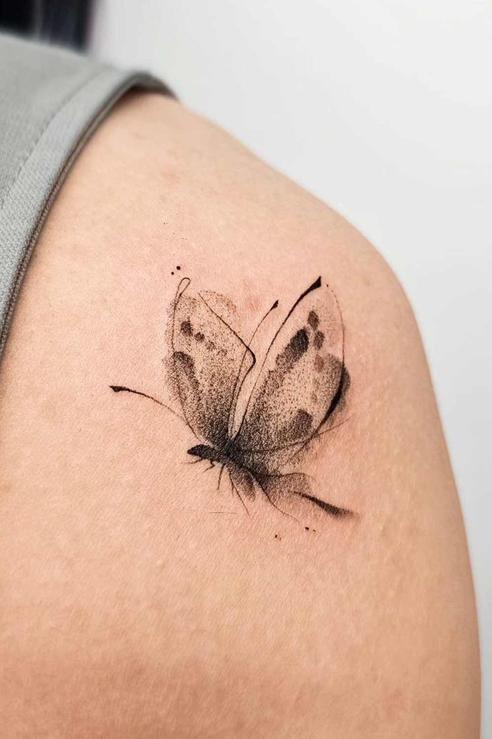 Butterfly tattoo on a shoulder with a soft, faded ink effect on wings