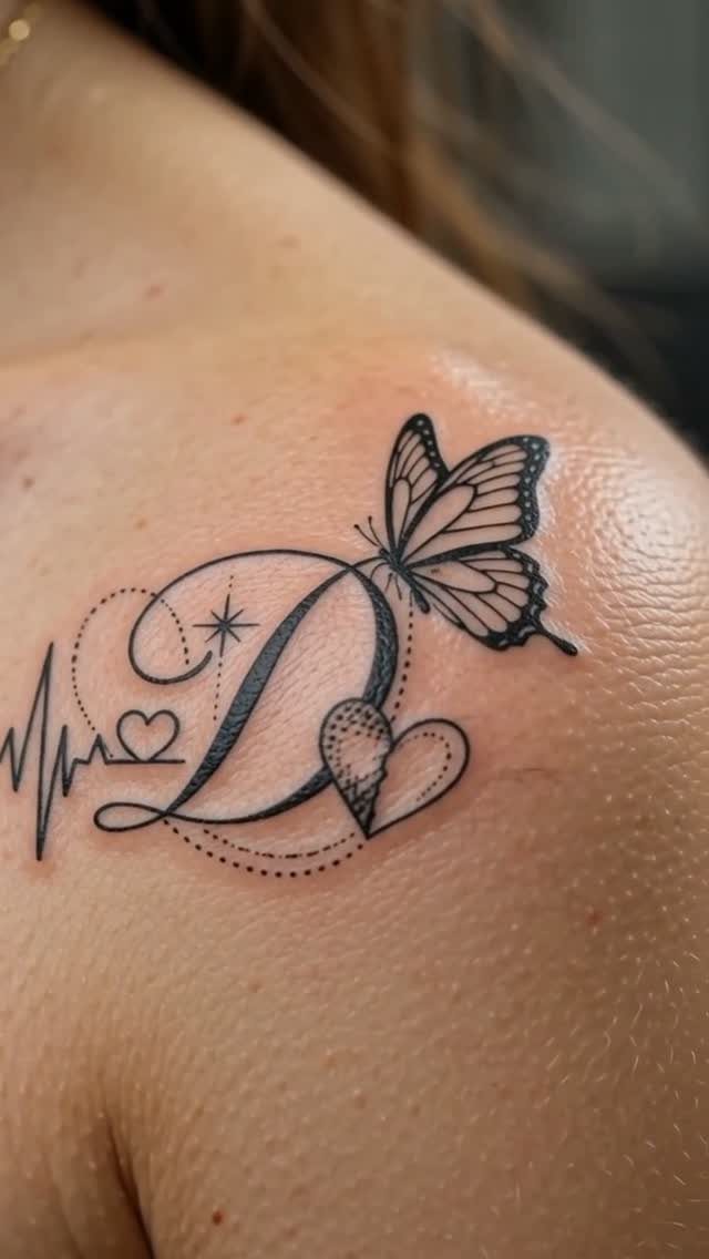 Butterfly tattoo on shoulder with a cursive letter D, heart, and heartbeat line.