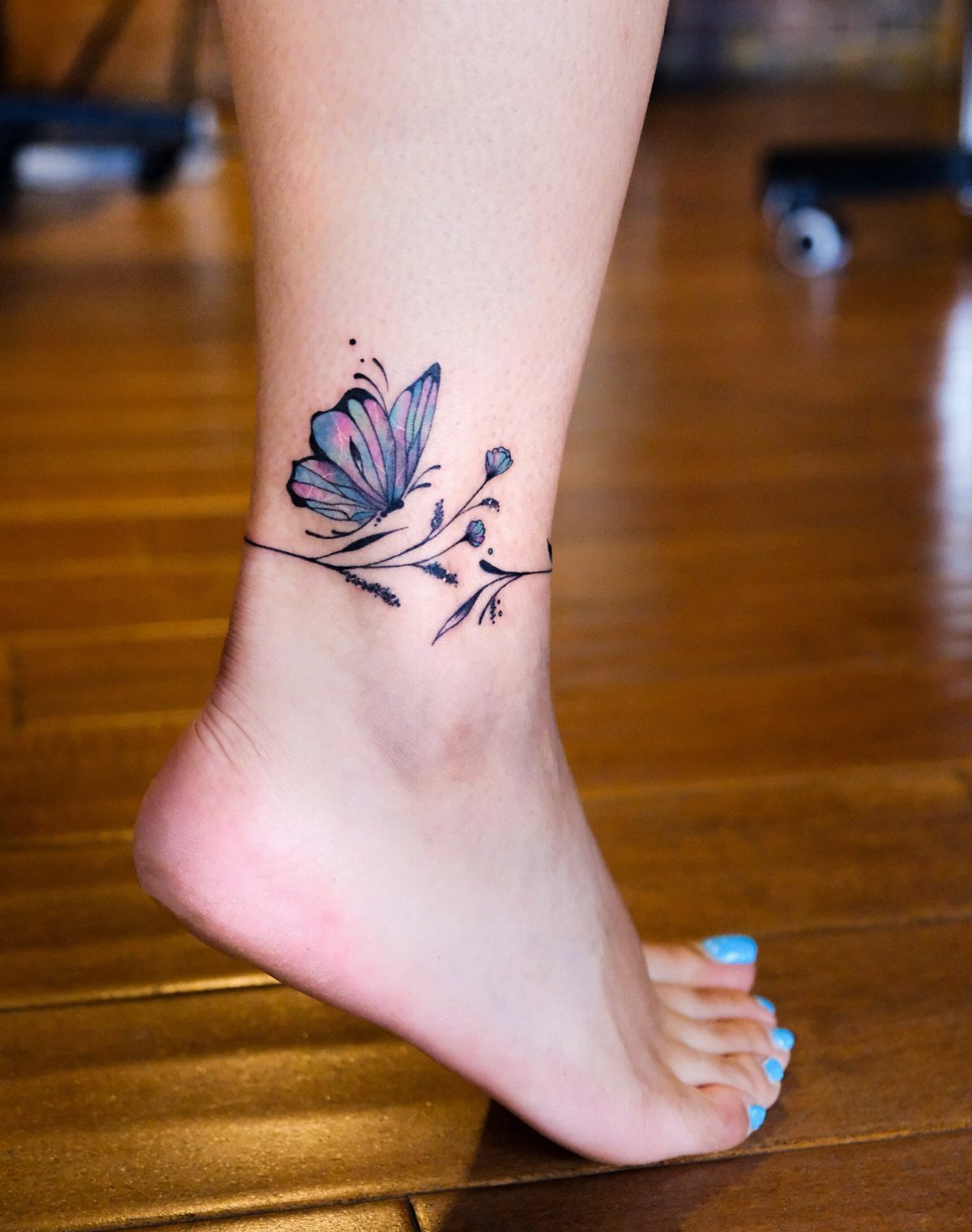 Blue and purple butterfly tattoo with floral accents on a person's ankle.