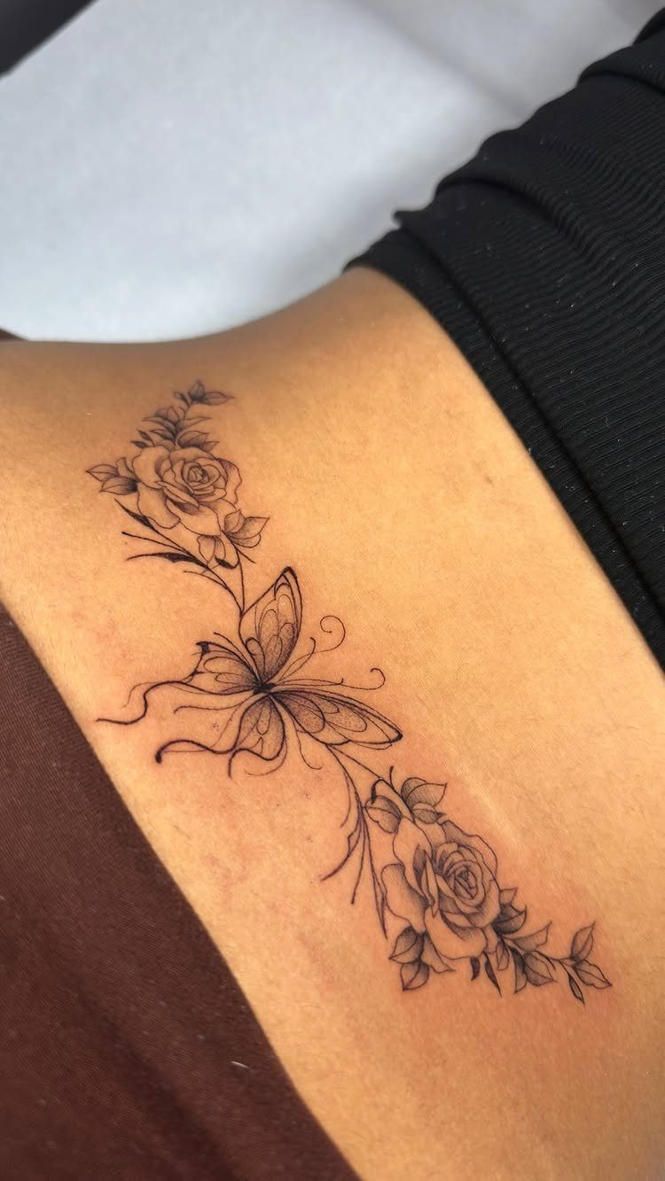 Butterfly tattoo with rose accents on a person's lower back in black ink.