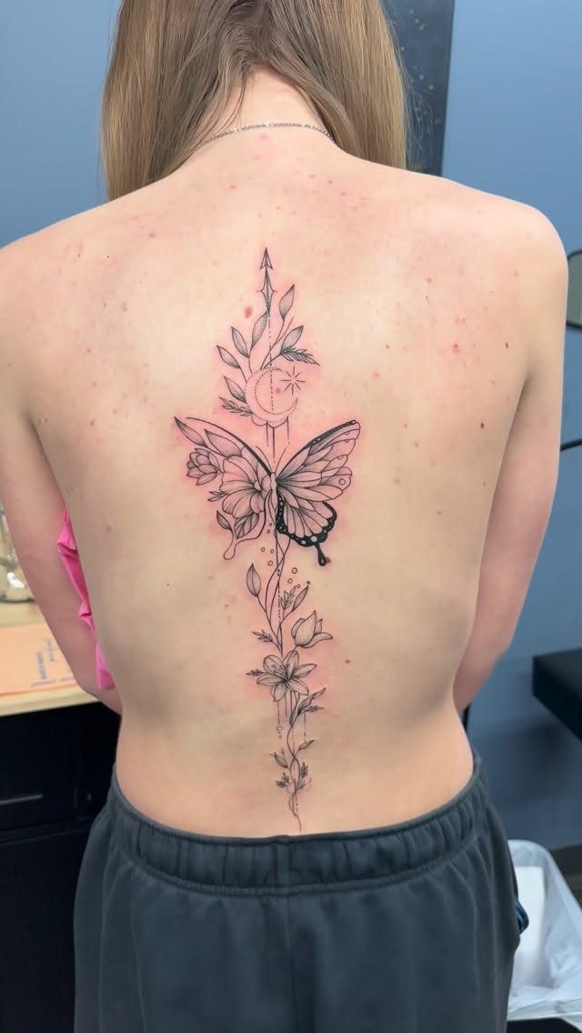 Butterfly tattoo with floral elements running vertically down a woman's spine