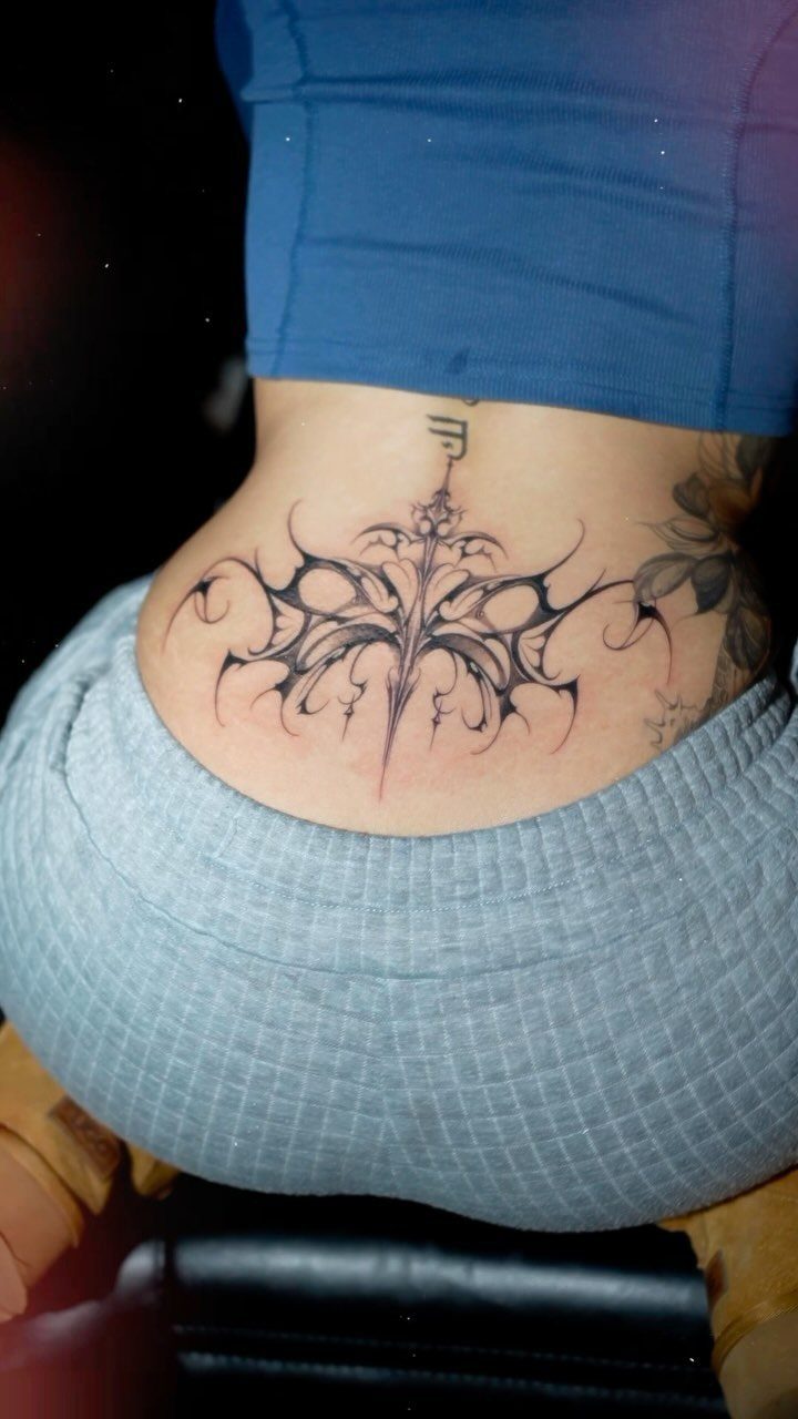 Symmetrical black ink butterfly tattoo on a person's lower back above grey pants