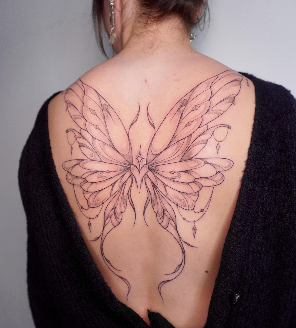 Large butterfly wing tattoo on a woman's back with ornate line art details