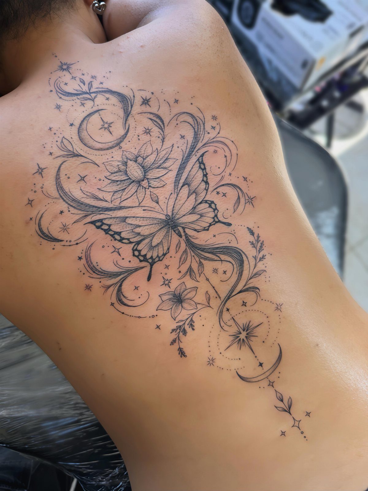 Butterfly tattoo on a back featuring stars, crescent moons, and floral swirls.