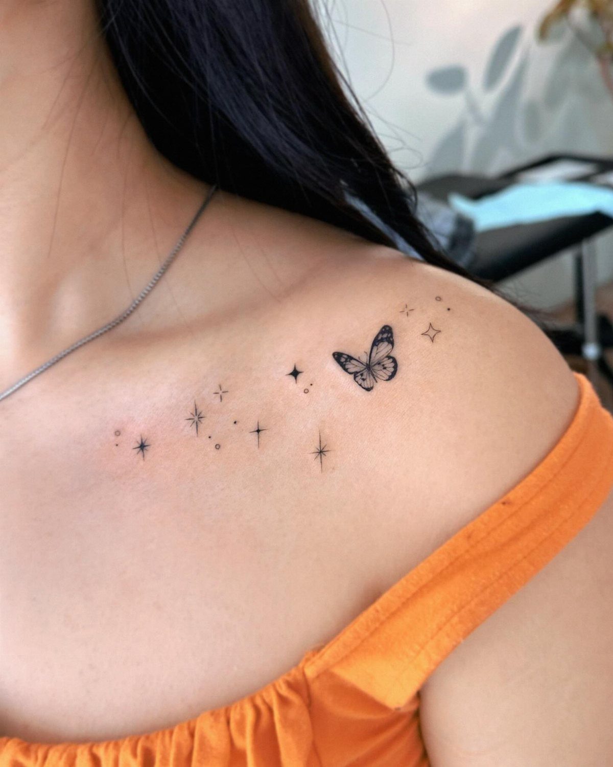 Small black butterfly tattoo with stars on a woman's collarbone and shoulder.
