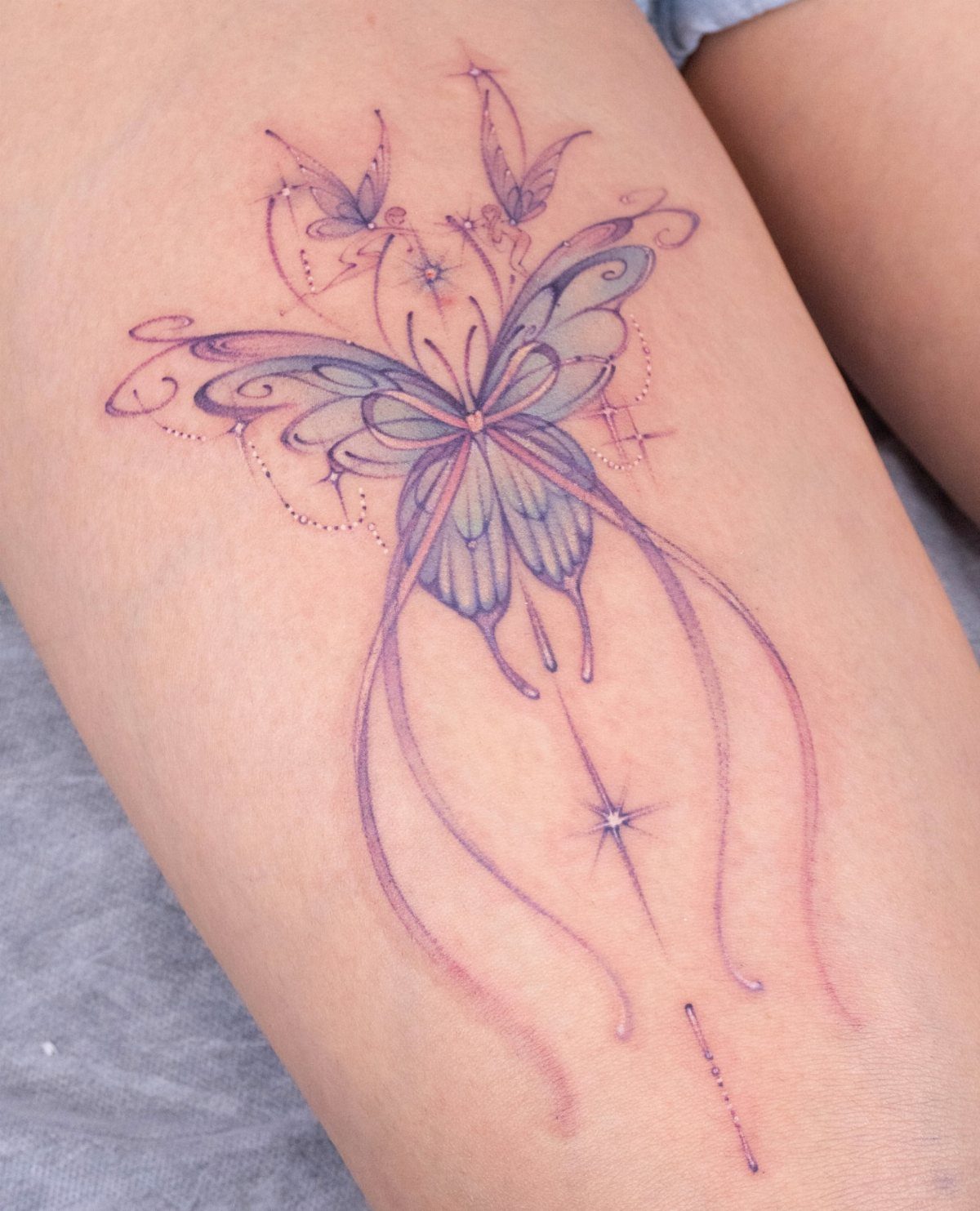 Stylized butterfly tattoo with blue and purple hues and mystical sparkles on skin