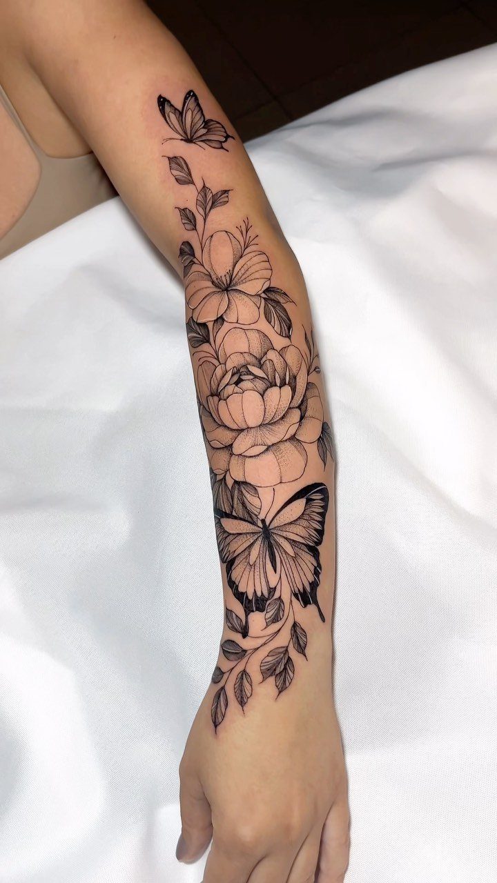 Black ink forearm tattoo of butterflies and large blooming flowers with leaves.