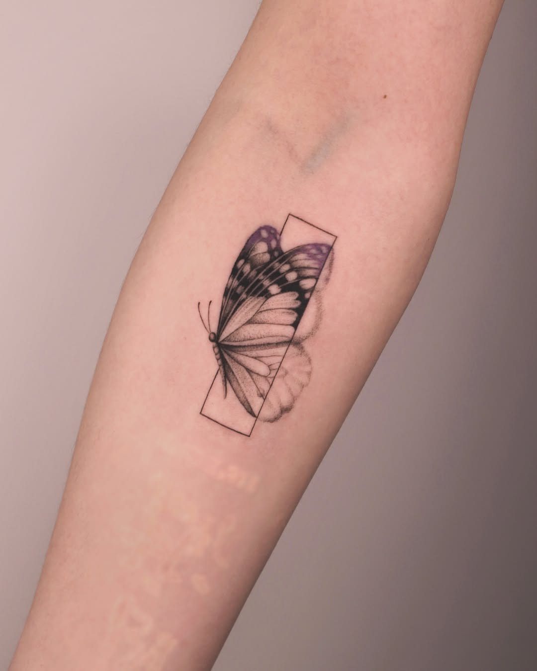 Butterfly tattoo on a forearm featuring purple wings and a geometric frame.