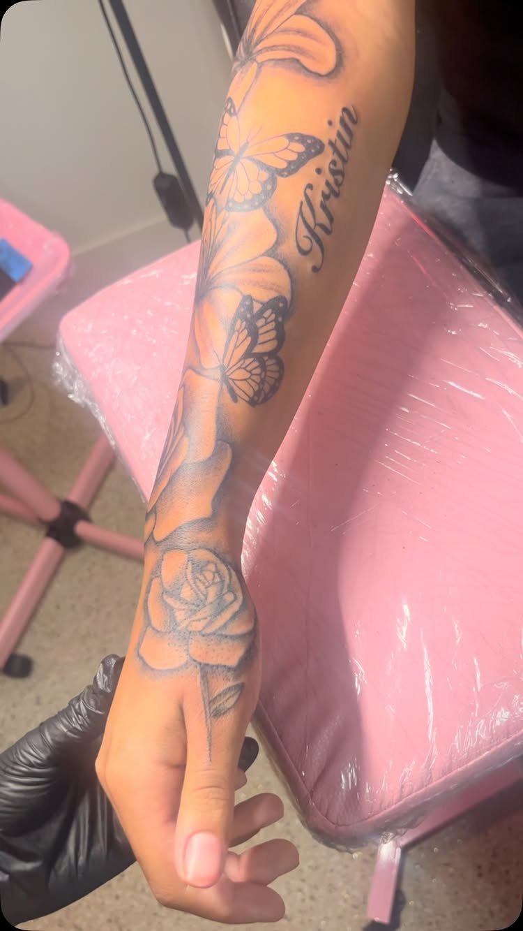 Forearm tattoo featuring multiple butterflies, a rose on the hand, and cursive text.