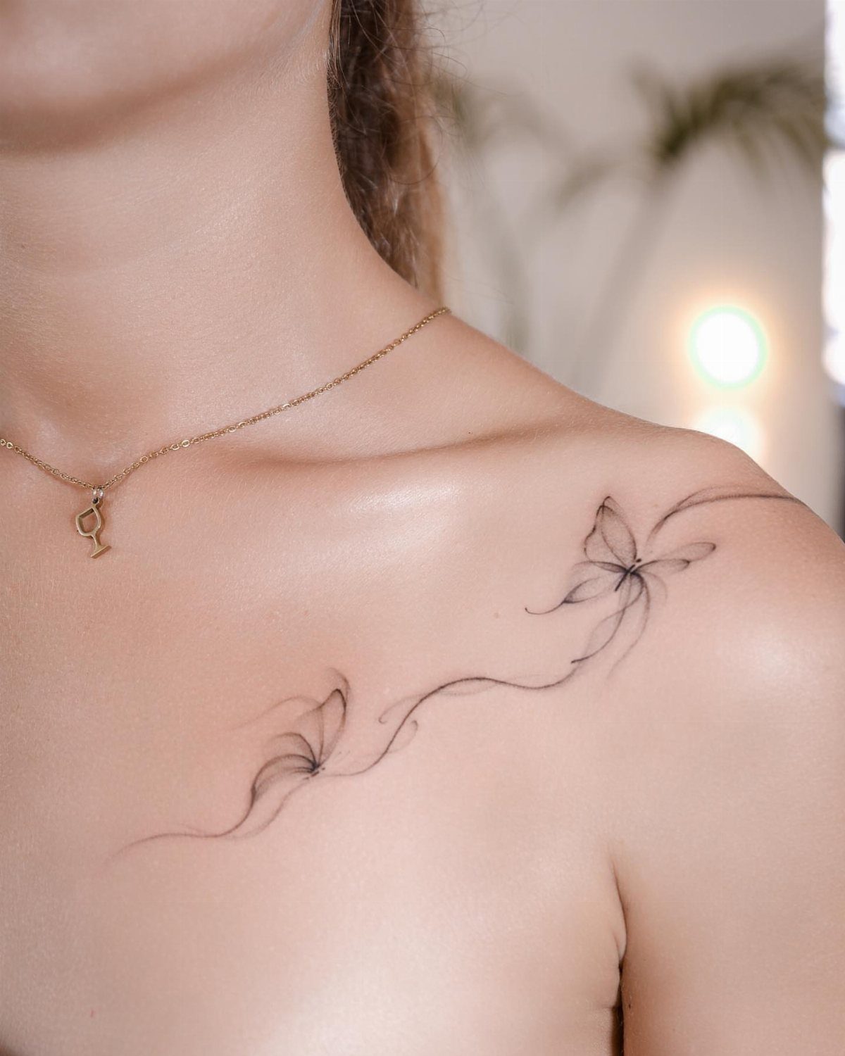 Minimalist line art butterfly tattoos on a woman's shoulder and collarbone area.