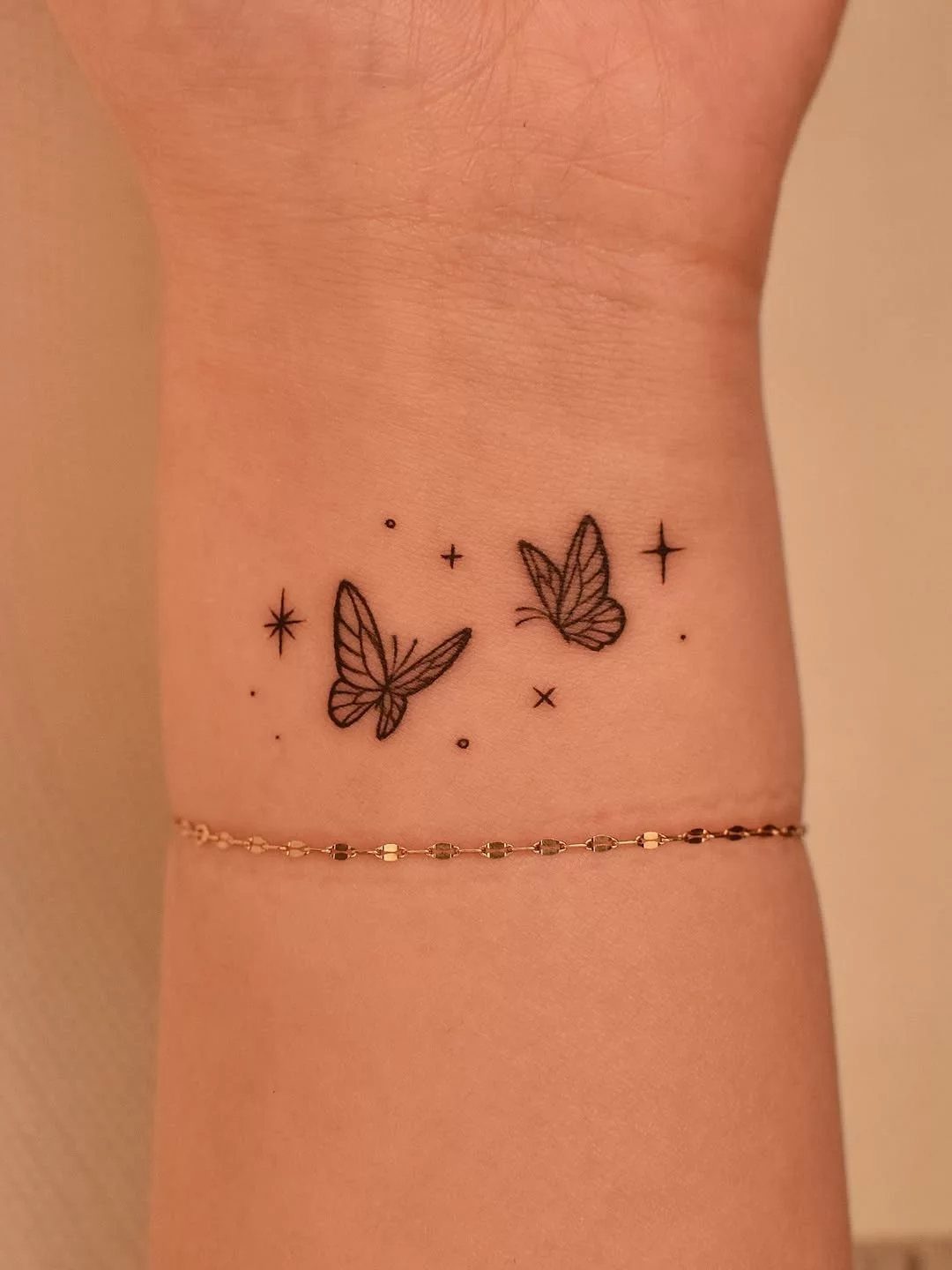 Two tiny black butterfly tattoos with stars on a person's inner wrist.