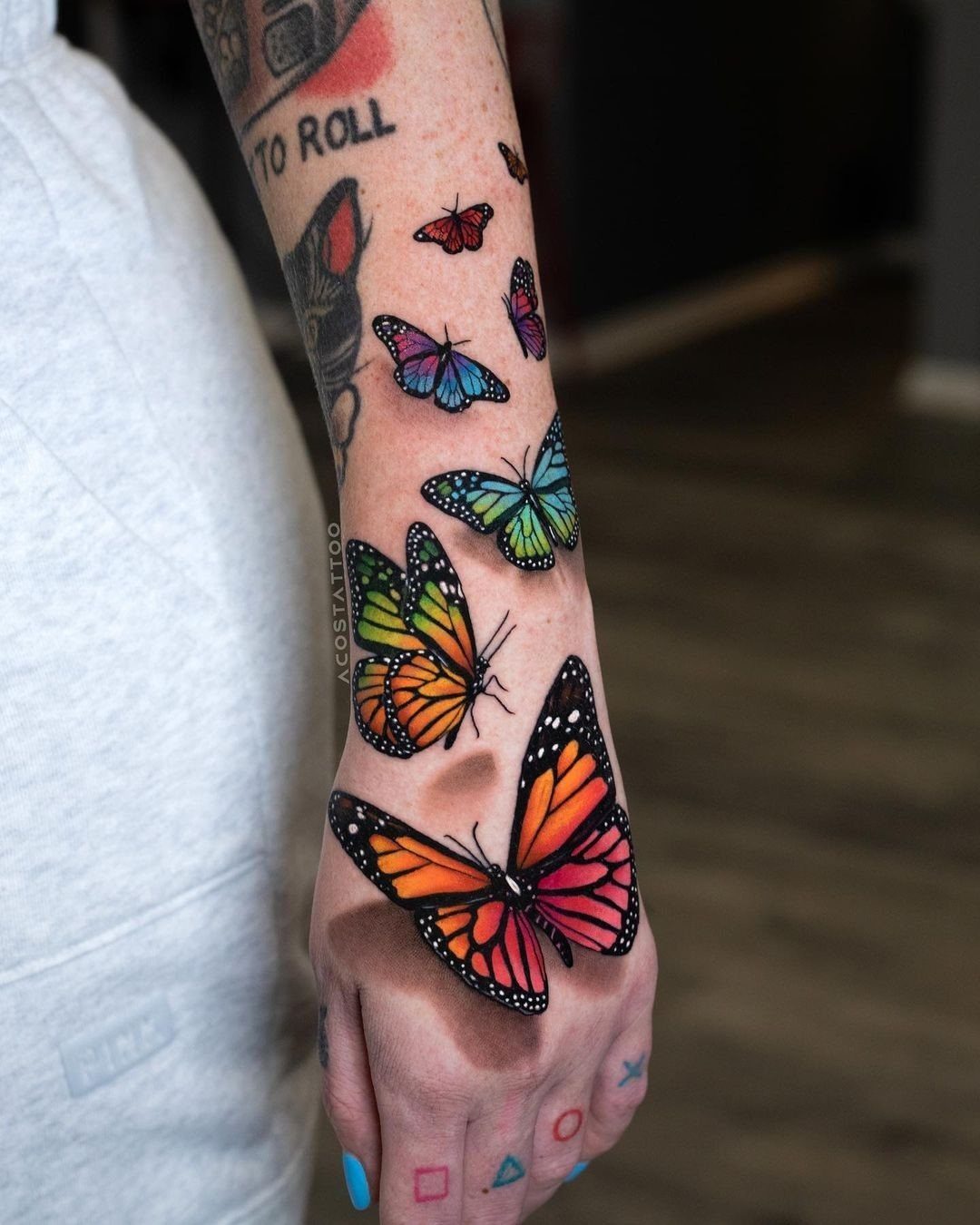 Colorful butterfly tattoos of various sizes and colors on a person's forearm.