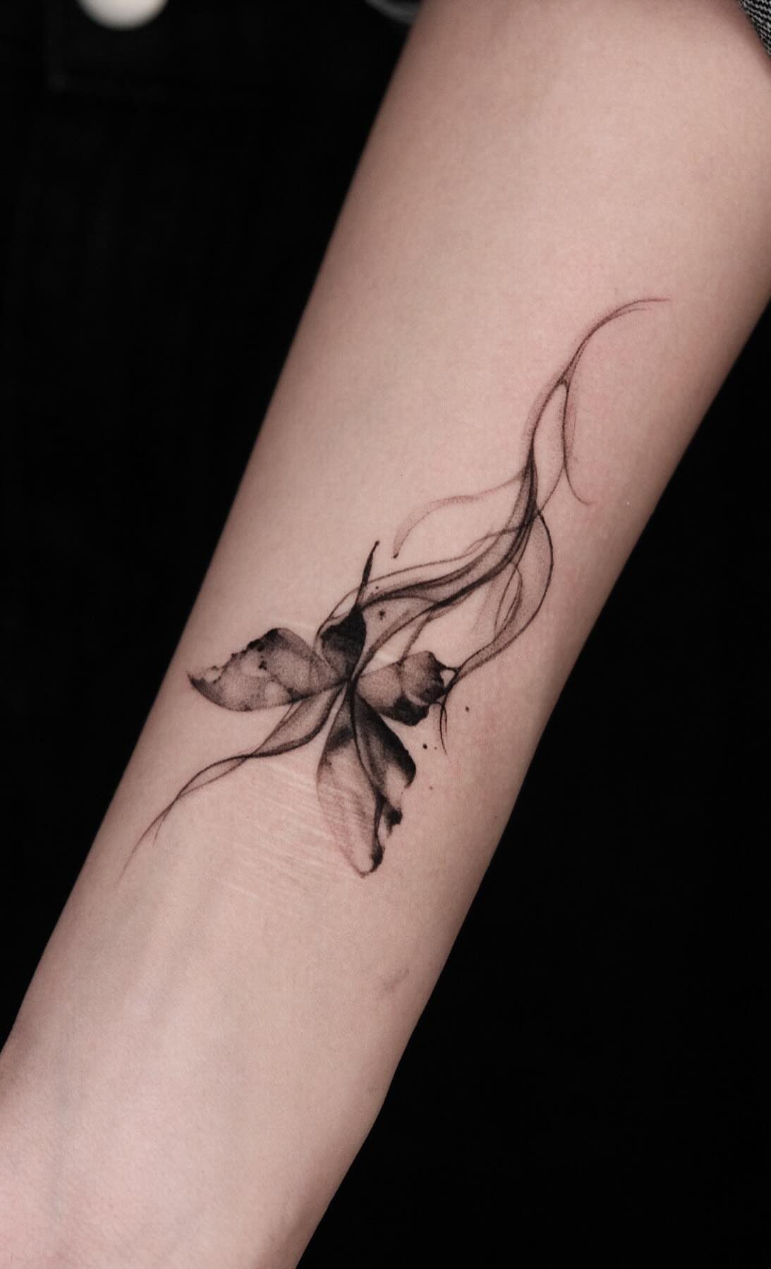Abstract black ink butterfly tattoo with flowing lines on a person's forearm