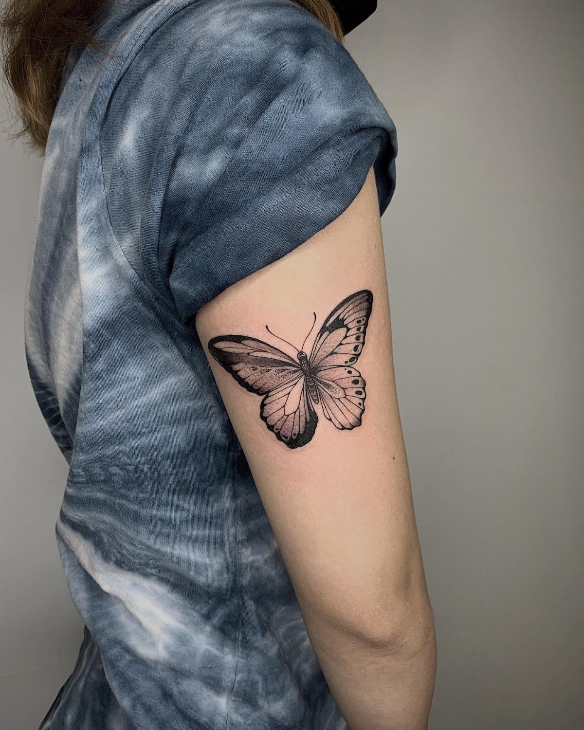 Black ink butterfly tattoo angled on a person's upper arm