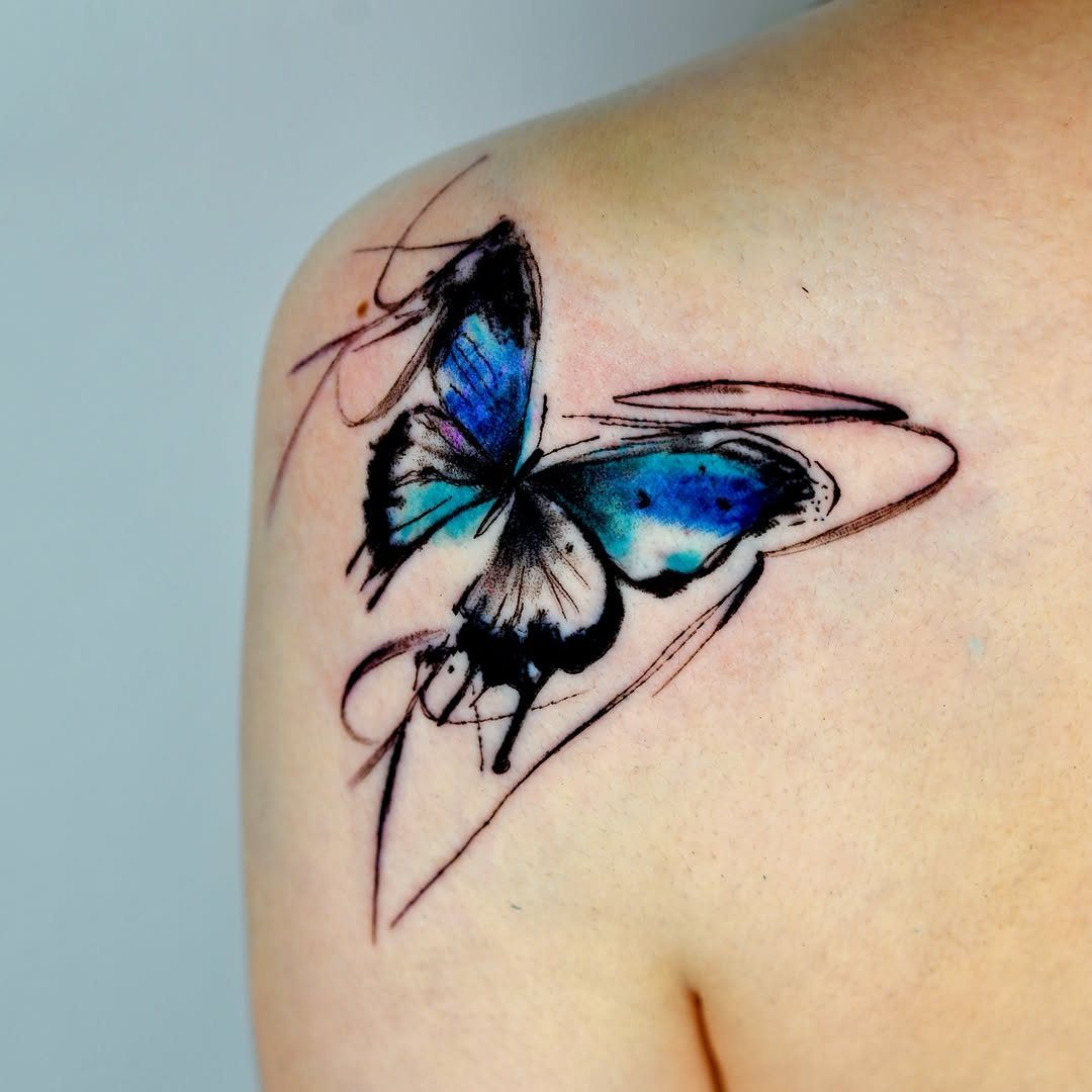 Blue and black butterfly tattoo with artistic brush strokes on an upper arm