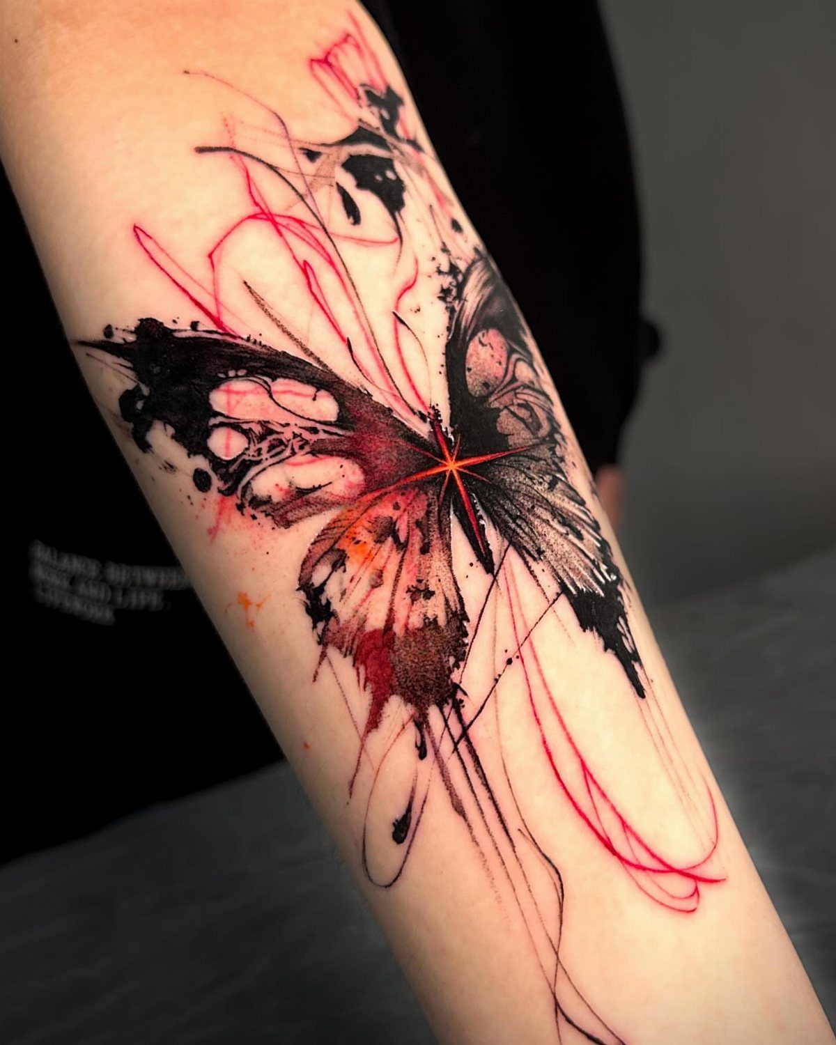 Butterfly tattoo on forearm with red and black ink and abstract splatters