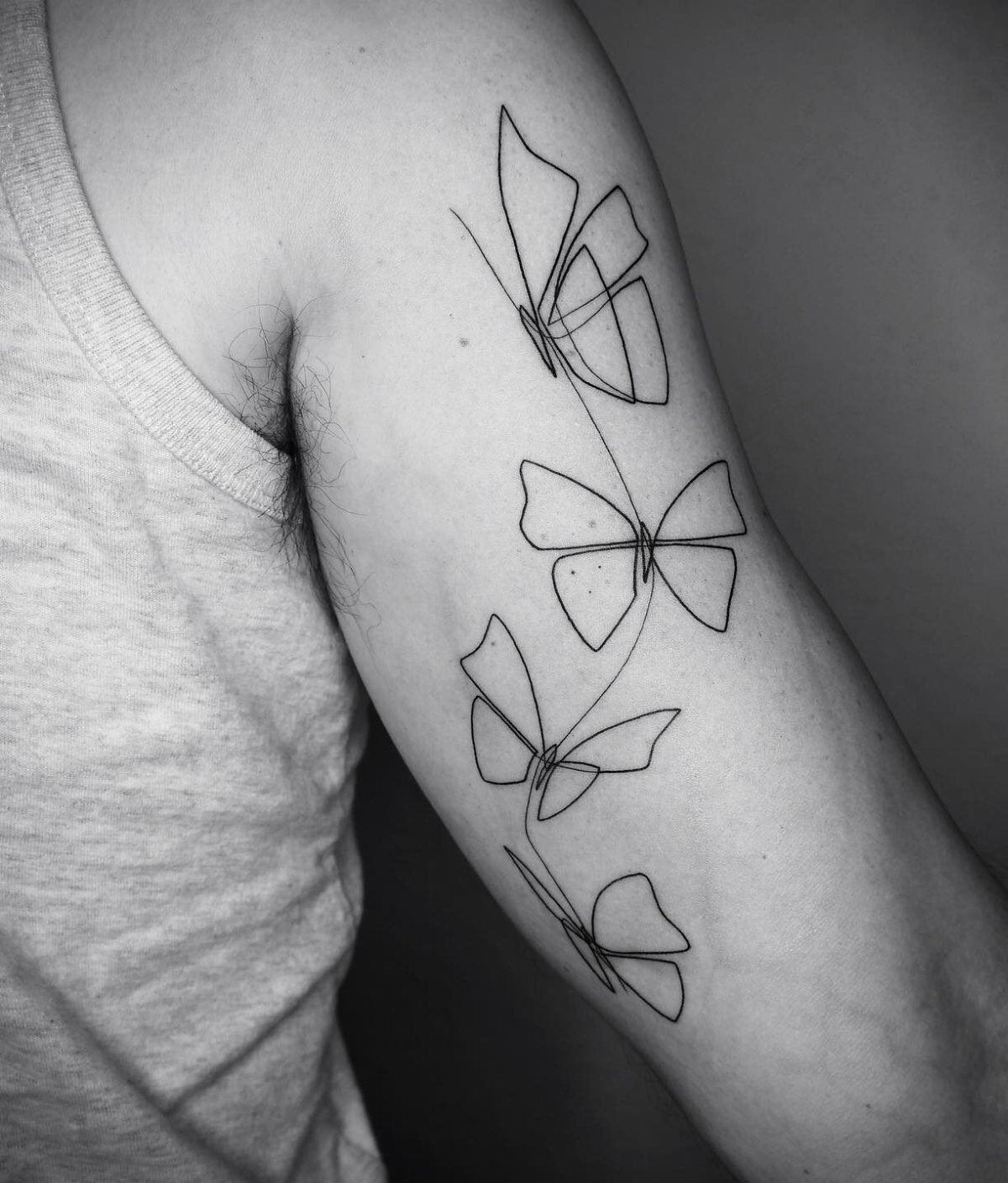 Continuous line tattoo of four butterflies flowing down a person's upper arm.