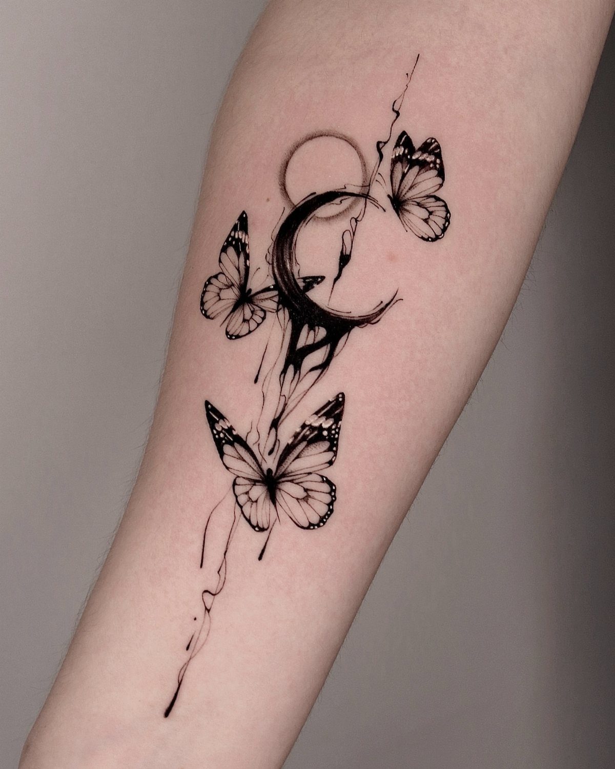 Black ink butterfly and crescent moon tattoo flowing down a person's forearm
