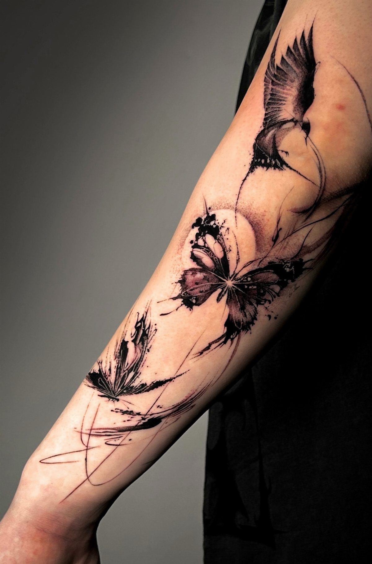 Butterfly, bird, and leaf tattoos on an arm connected by flowing black ink lines.