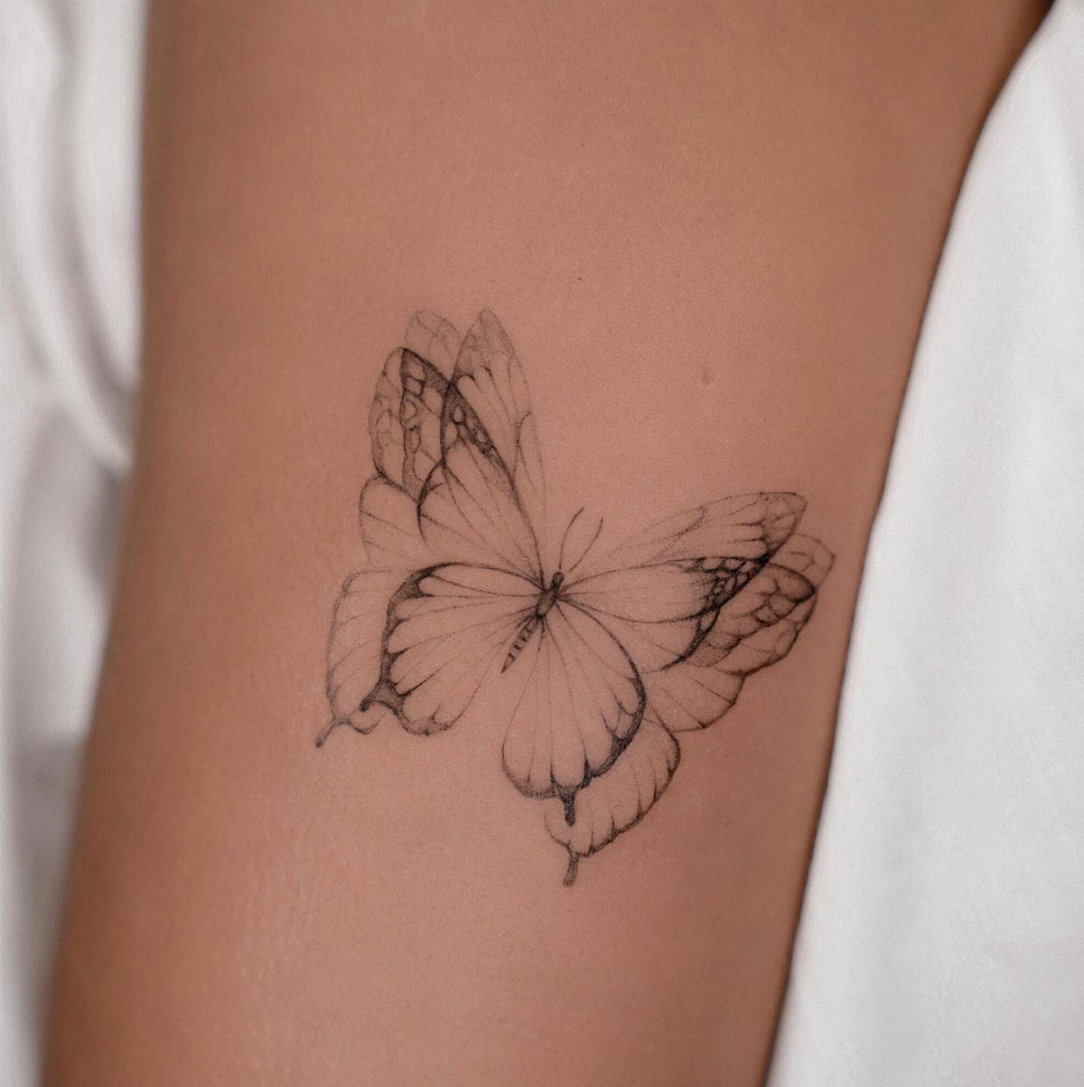 Butterfly tattoo on an arm featuring multiple layered thin outlines of wings.