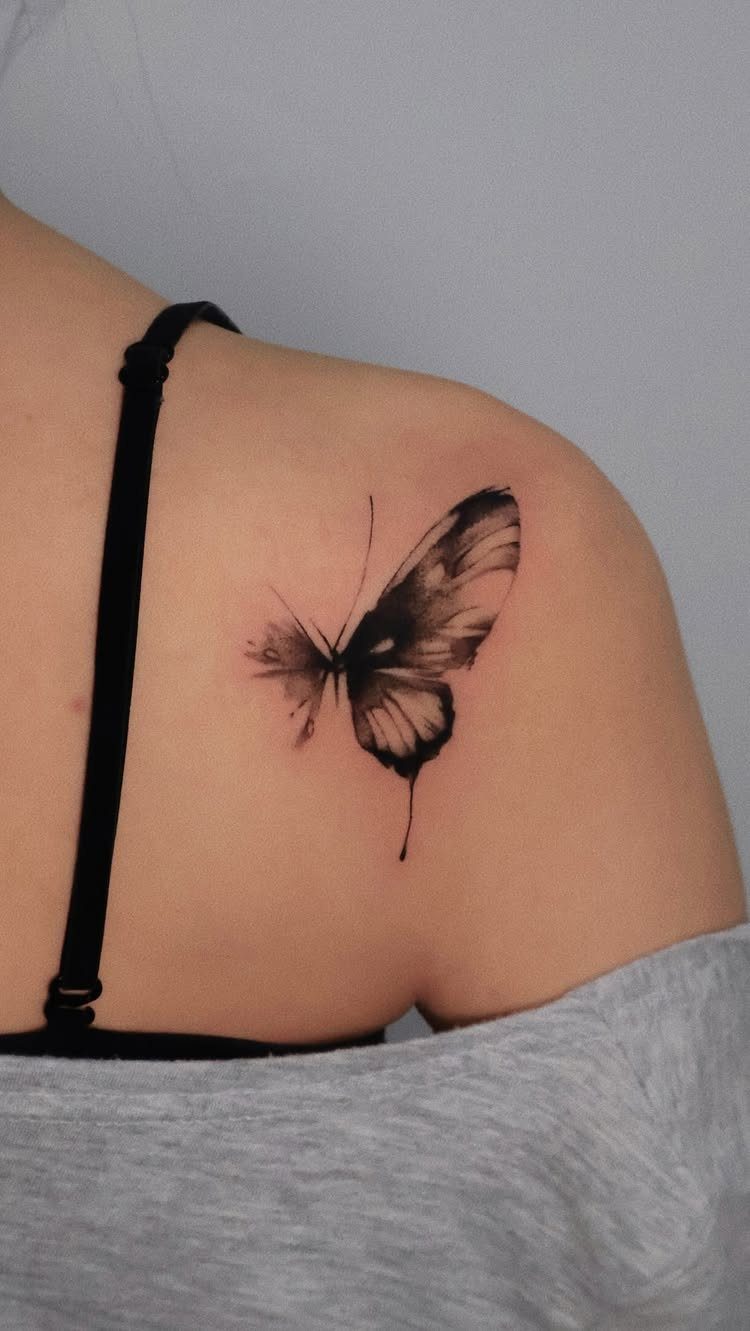 Butterfly tattoo on upper arm with soft black gradient shading and realistic wings