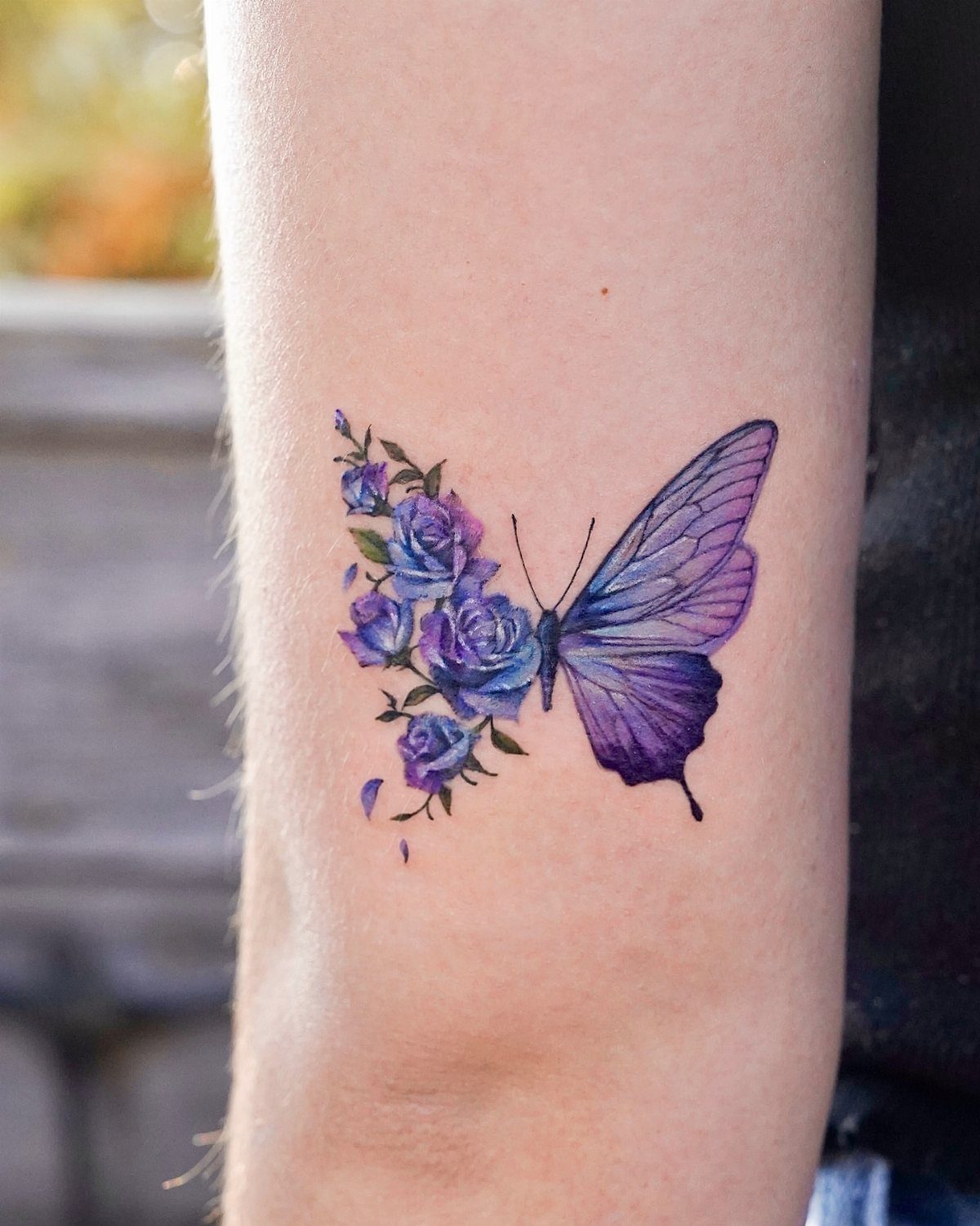 Purple butterfly tattoo on forearm with one realistic wing and one floral wing